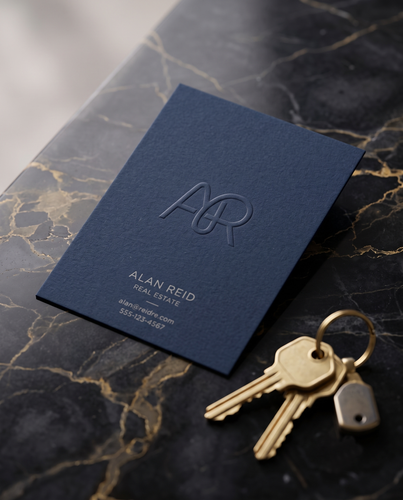 Blind embossed business card in navy cardstock with a raised "AR" monogram for a real estate agent, styled with brass keys on a dark marble surface.