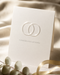 Raised spot UV greeting card in matte ivory cardstock with a glossy interlocking rings design and "Congratulations" lettering, styled with white eucalyptus and gold ribbon. Years old