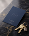 Blind embossed business card in navy cardstock with a raised "AR" monogram for a real estate agent, styled with brass keys on a dark marble surface.