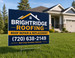 Coroplast yard sign for a roofing company, printed in full color with bold contact information, mounted on an H-frame stake in a residential front yard
