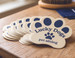 Die cut sticker shaped like a paw print for Lucky Dogs Pet Sitting, fanned out on a wood table with a grooming brush, bandana, and dog treats — custom die cut sticker example