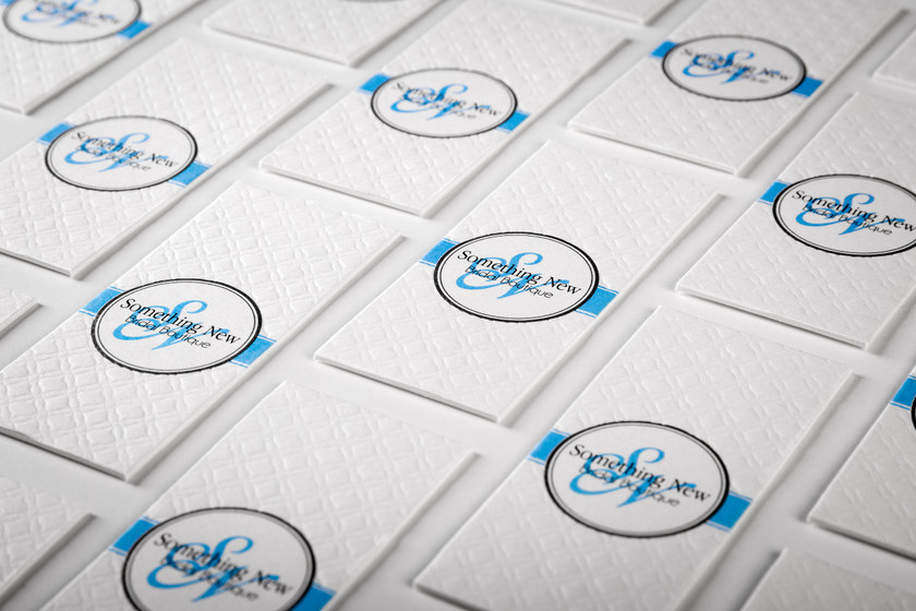 Blind embossed business cards arranged in a grid, each card featuring a small circular monogram with a blue-trimmed border detail.