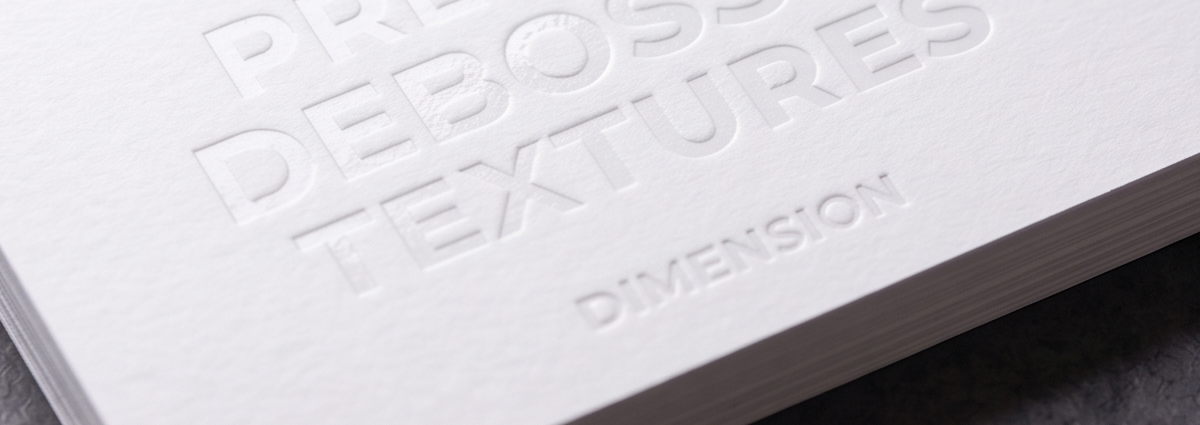 A blind debossed business card showing recessed lettering pressed into thick, uncoated white cardstock with no ink or foil, relying on light and shadow alone to reveal the design.