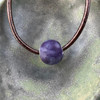 Shown in purple, this glaze is glossy. Cremation ash bead shown in purple on a dark brown leather cord.