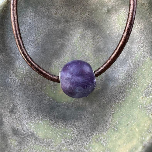 Shown in purple, this glaze is glossy. Cremation ash bead shown in purple on a dark brown leather cord.