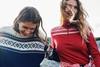 Dale of Norway Cortina Women's Base Layer Sweater, Raspberry/Off White, 93521-B_lifestyle image of two models laughing and wearing cortina patern in a red base layer and navy unisex crewneck sweater