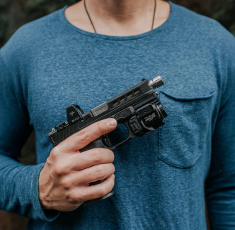 True Precision Glock 19 with stainless barrel, black slide and grip, being held by a man in a blue shirt.