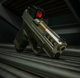 A Springfield Hellcat with a True Precision non-threaded FDE barrel and stainless Axiom slide sitting on top of raw steel bars