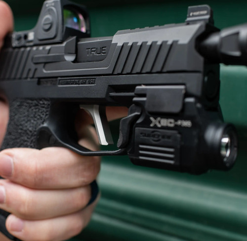 Close up picture of a Sig P365 with a True Precision threaded duty barrel, and slide on a green corrugated metal background