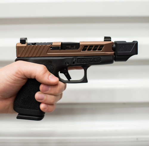 True Precision Glock 43X with copper slide and black threaded barrel and Compensator being held against white metal background.
