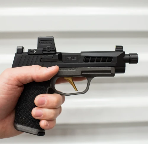 A Sig P365 XL with a True Precision Threaded black nitride barrel and Axiom slide, and copper TiCN True flat trigger being held against grey corrugated metal