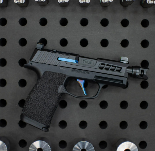 Sig P365 with True Precision Black nitride threaded barrel, axiom slide and cobra comp and blue True Trigger and OEM extractor on a black background with holes and barrel blanks 