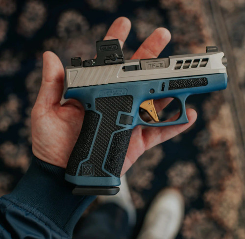 Glock 43X with non-threaded stealth grey barrel, being held over carpeted background.