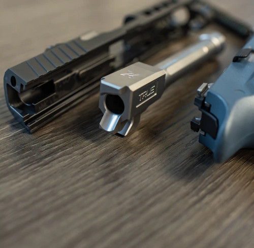 A True Precision Sig P320 Compact threaded barrel sitting outside the slide and lower on a wooden table