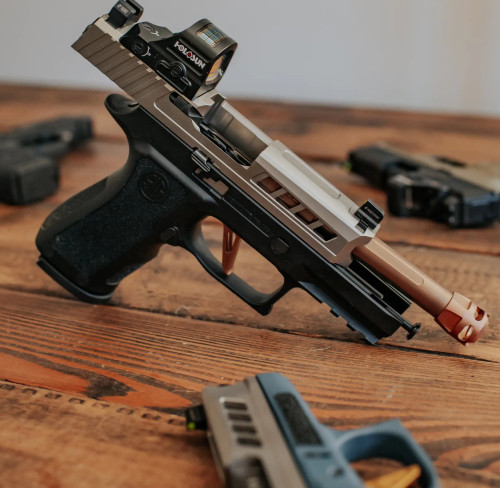 A Sig P320 Compact with True Precision threaded barrel and Y-Type Micro compensator in Copper TiCN, and a Satin stainless Axiom slide, on a wood table with other guns in the background