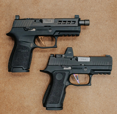 Two Sig P320 Compacts laying on a wooden table, one threaded, one non-threaded True Precision barrels 