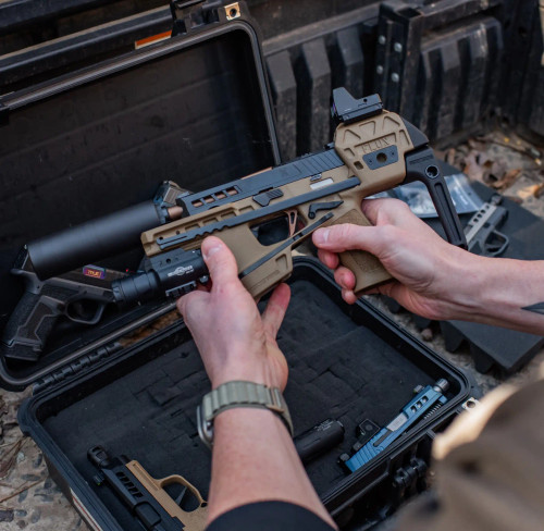 The side profile of a Sig P320 Compact FLUX Raider, with True Precision threaded copper TiCN barrel, and black suppressor, with a gun case in the background