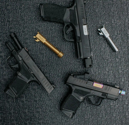Three Springfield Hellcats laid out on a black background all with either threaded or non-threaded True Precision barrels of various coatings