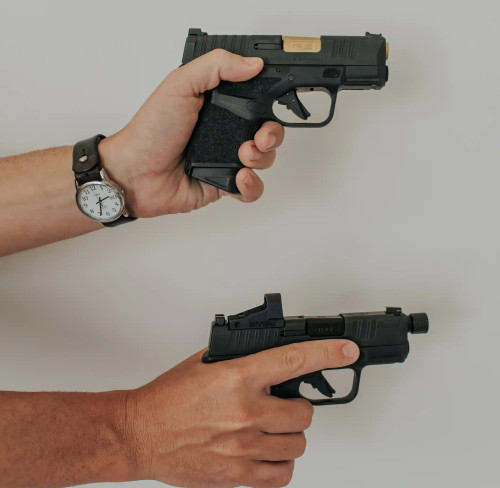Two Springfield Hellcats, with True Precision gold TiN  non-threaded barrel and black nitride threaded barrel being held one over the other over a grey background
