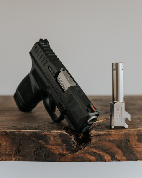 A Springfield hellcat with True Precision non-threaded stainless barrel sitting on a wooden table with a grey background