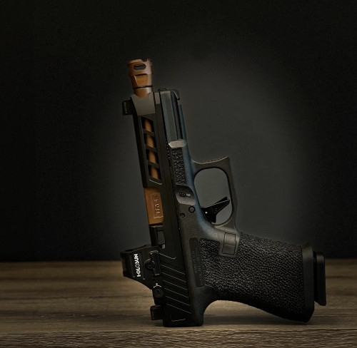 True Precision Glock 19 with black slide, copper threaded barrel, and black on black flat trigger, pointing up.