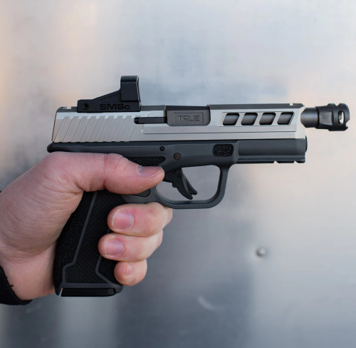 True Precision Springfield Hellcat Pro with stainless slide and black threaded barrel being held over silver background.