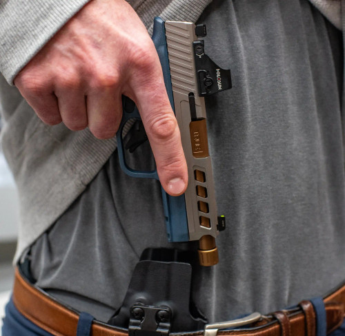 A Springfield Hellcat Pro with True Precision threaded barrel in copper TiCN, and stainless Axiom slide, being taken out of a holster