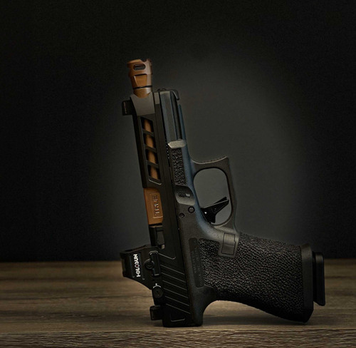 A Glock 19 with True Precisions Black DLC slide, Copper coated threaded barrel, Y-Type Micro Compensator and hand stippled lower. Sitting on a  wooden table with a black background.