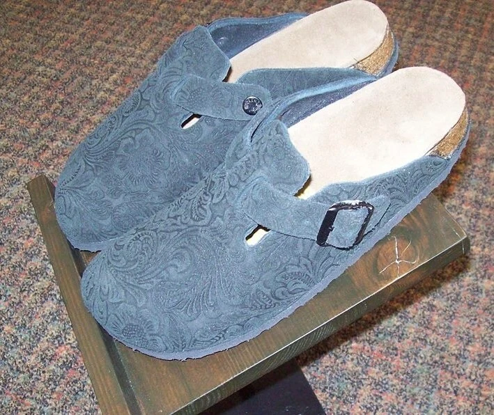 Teal Birkenstock clogs with an embossed floral pattern and adjustable buckle straps.