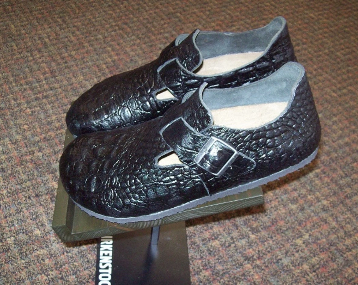 Black crocodile-textured Birkenstock shoes with adjustable buckle straps and closed heels.
