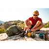 Man cooking breakfast with a Kelty Asher 65 backpack at his side