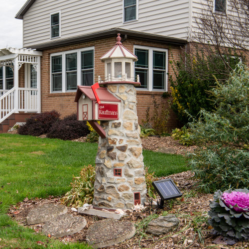 Amish handcrafted stone lighthouse with mailbox in flower bed by road.