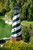 Cape Hatteras garden lighthouse replica in flower bed on bank of a pond.