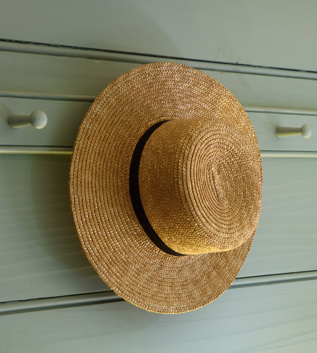 Amish straw hat hanging on wooden peg rail
