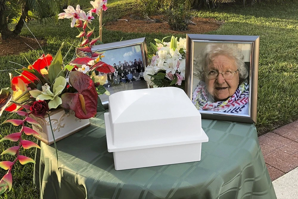 An urn vault on a draped table at a graveside service, with flowers and portraits