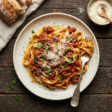 Overhead shot of fresh homemade pasta topped with rich Bolognese sauce and golden garlic bread with herbs and butter on a rustic wooden table