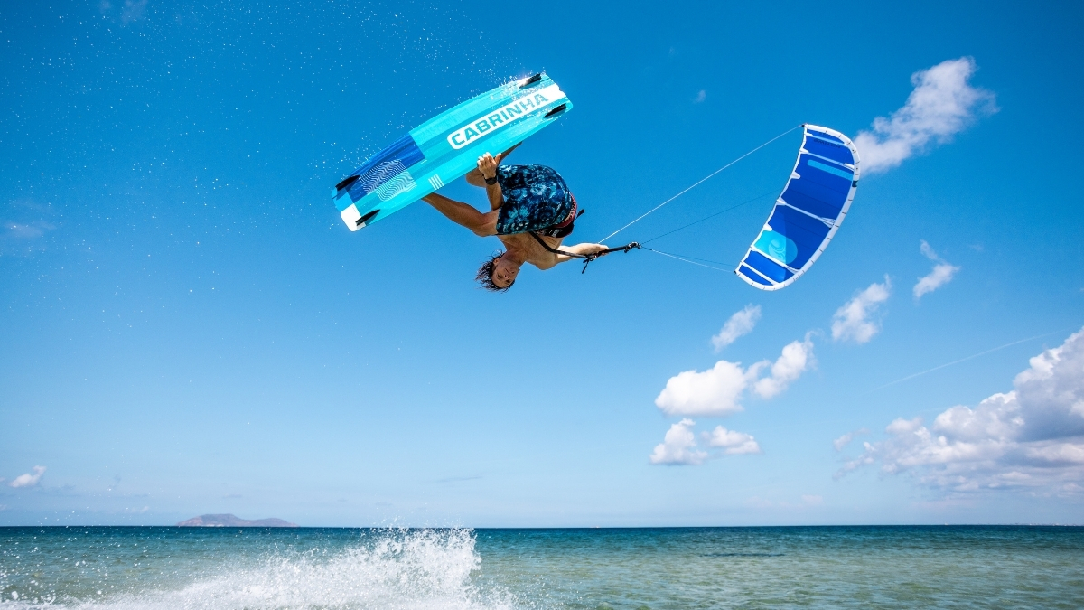 2026 Cabrinha Switchblade Apex rider inverted mid-air holding a Cabrinha twin tip over open water