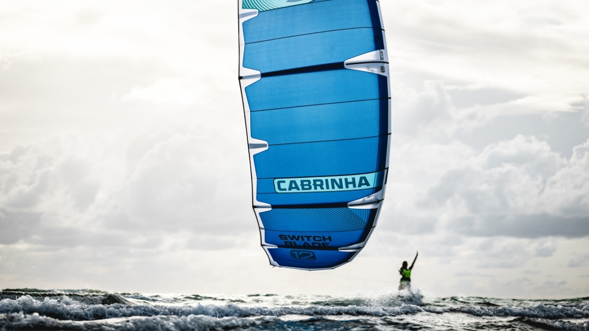 2026 Cabrinha Switchblade Apex 12m kite flying overhead with a rider in the surf below