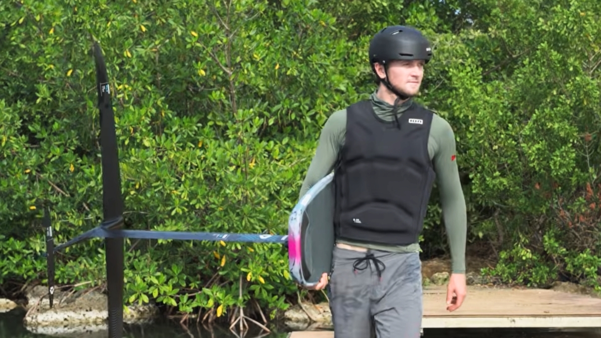 Pump foil rider wearing impact vest and helmet on a dock with foil board ready to dockstart