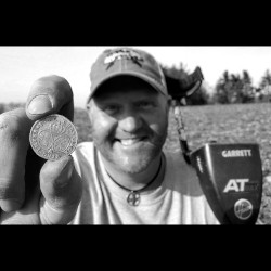 Black and White Image of The Hoover Boys' Kurt Franz Holding Coin Find Between Thumb and Forefinger with Garrett AT Max Metal Detector on His Shoulder