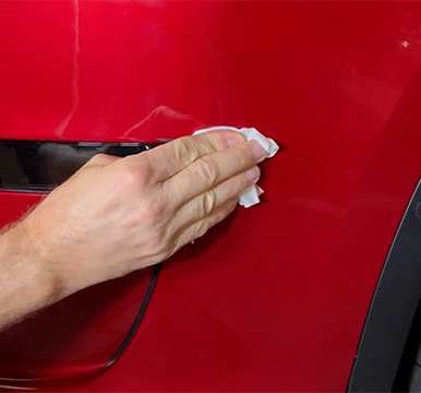Hand cleaning a scratch on a red vehicle panel before applying touch up paint