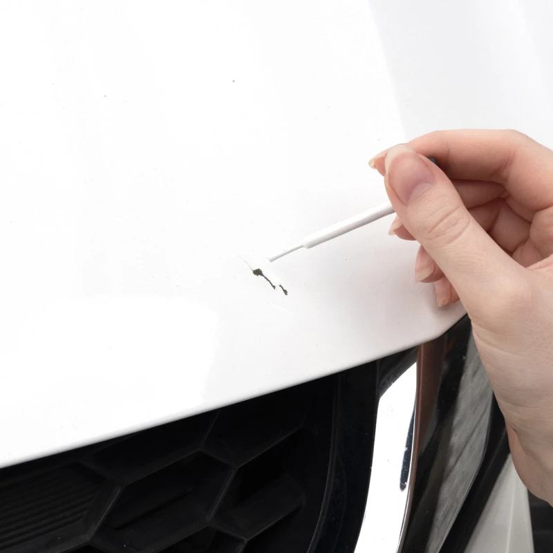  Hand applying colorcoat with a fine brush to scratches on a white vehicle panel