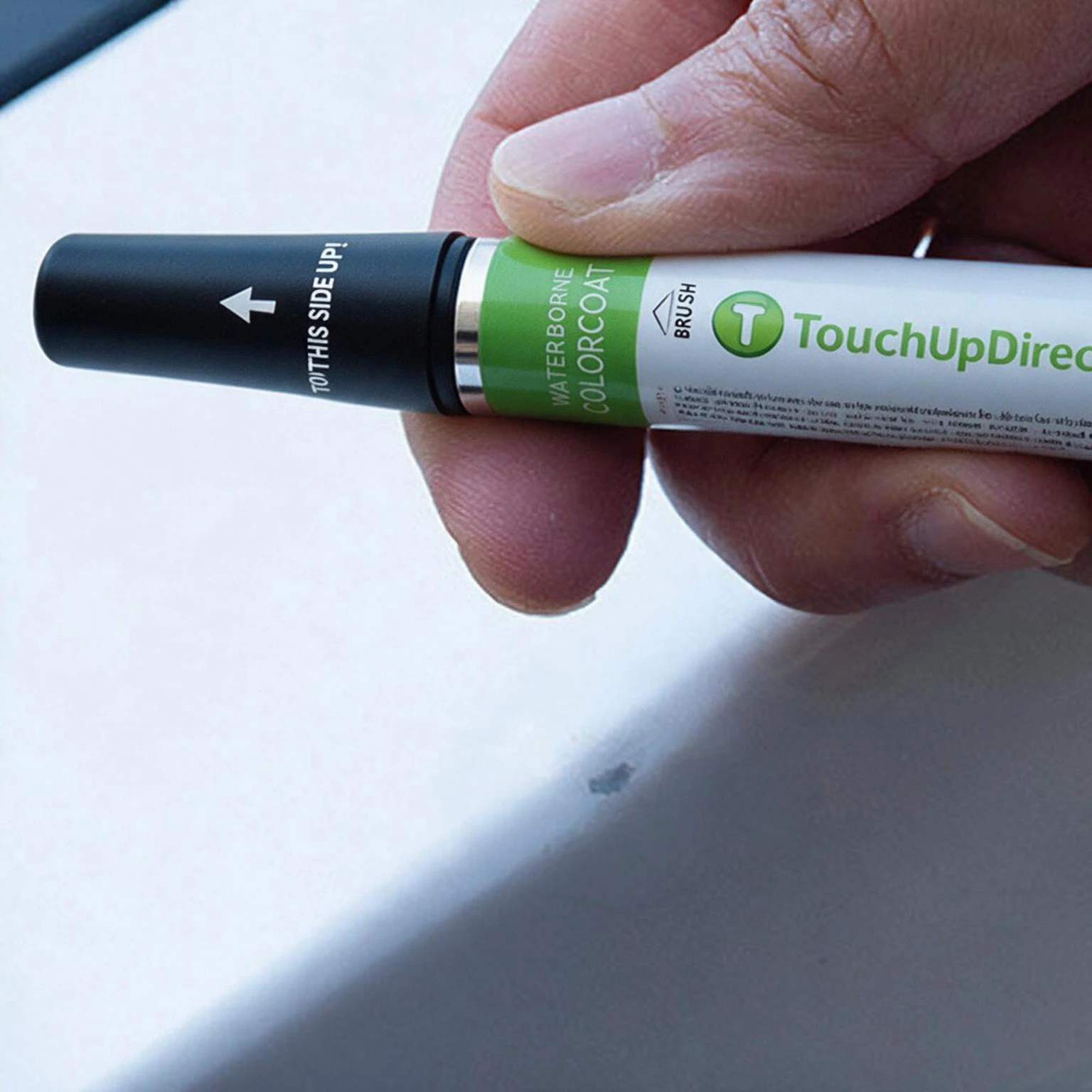 Hand holding a TouchUpDirect colorcoat brush bottle before shaking the paint