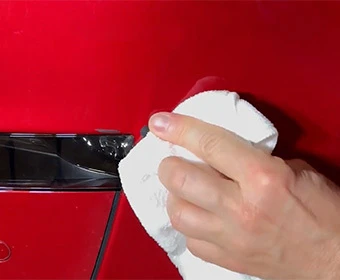 Hand wiping the damaged area of a red vehicle with a white cloth