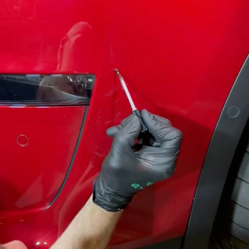 Gloved hand applying clearcoat with a fine brush to a repaired area on a red vehicle panel