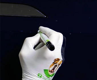 Gloved hand applying colorcoat with a TouchUpDirect pen to a small paint chip