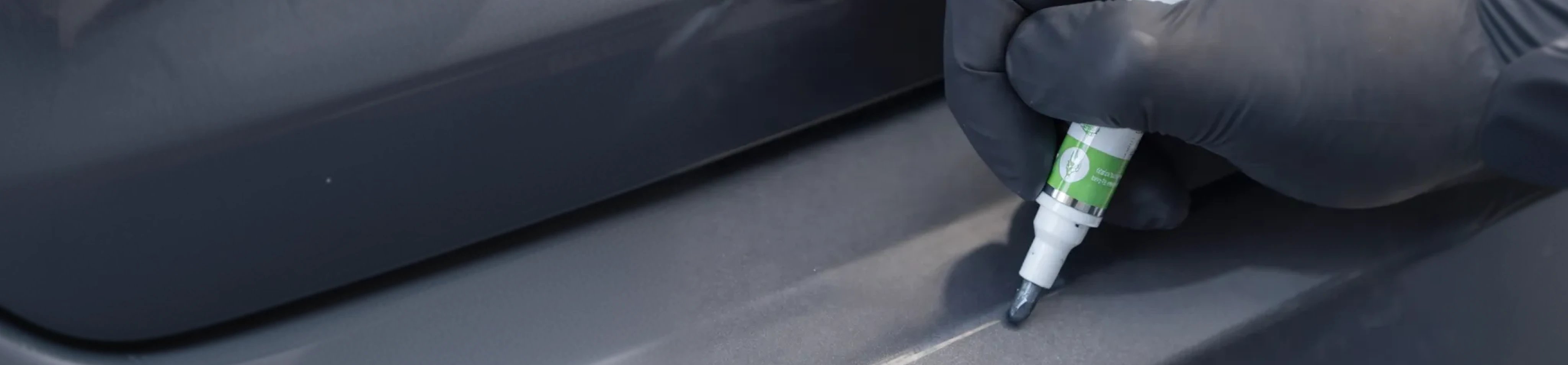 Gloved hand applying automotive touch up paint to a vehicle panel.