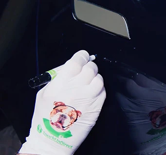 Gloved hand dragging a touch up paint pen along a scratch instead of dabbing the paint