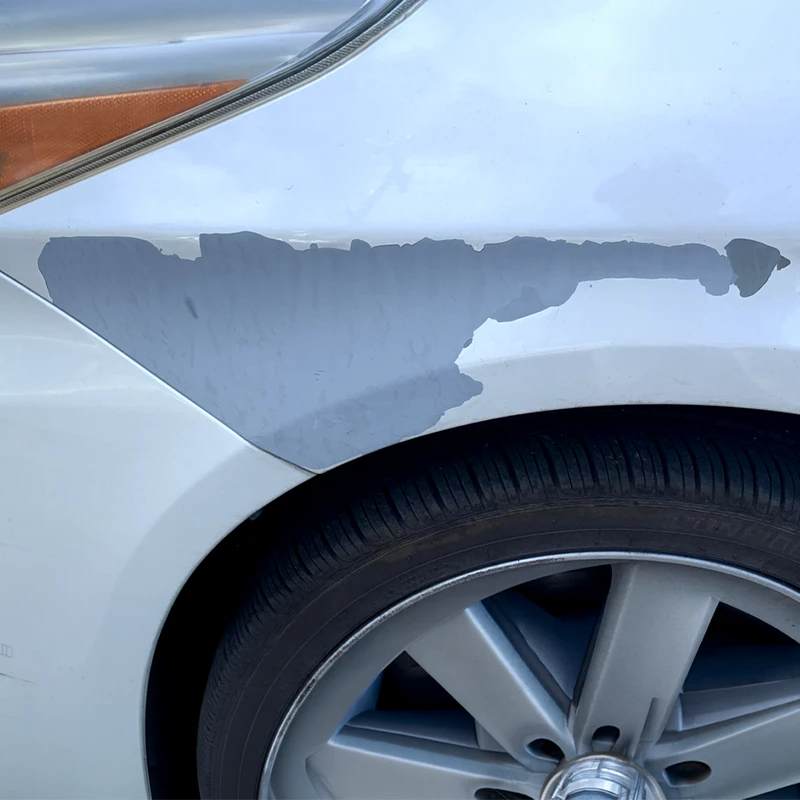Large area of gray paint peeling from a white vehicle fender above the wheel.
