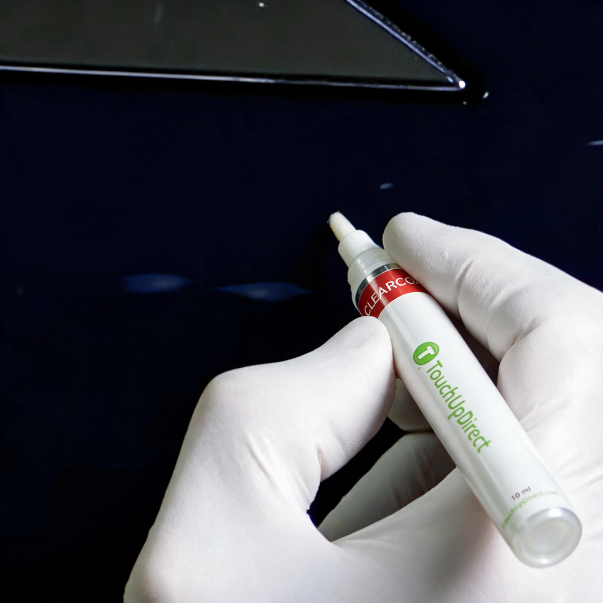 Gloved hand applying clearcoat with a TouchUpDirect paint pen over repaired rock chips on a dark blue vehicle panel.